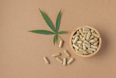 cbd pills on brown background with cannabis leaf