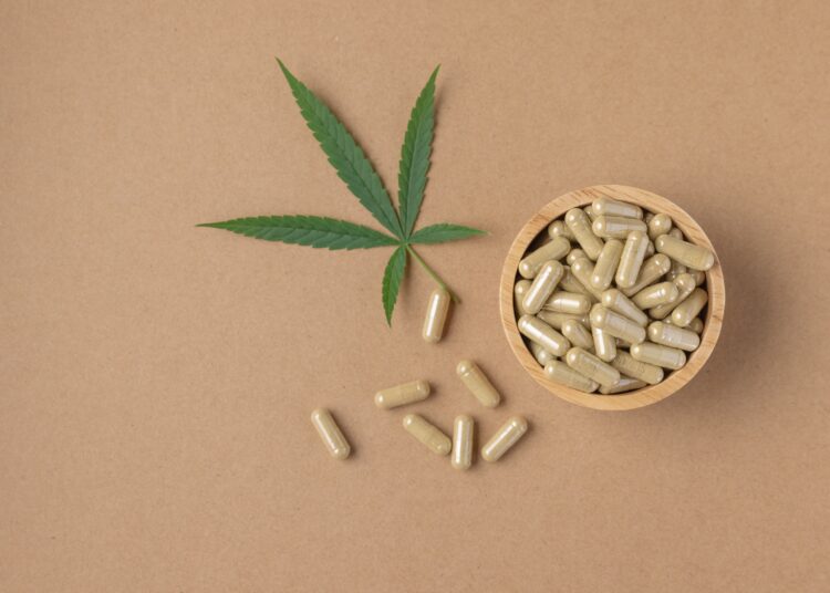 cbd pills on brown background with cannabis leaf