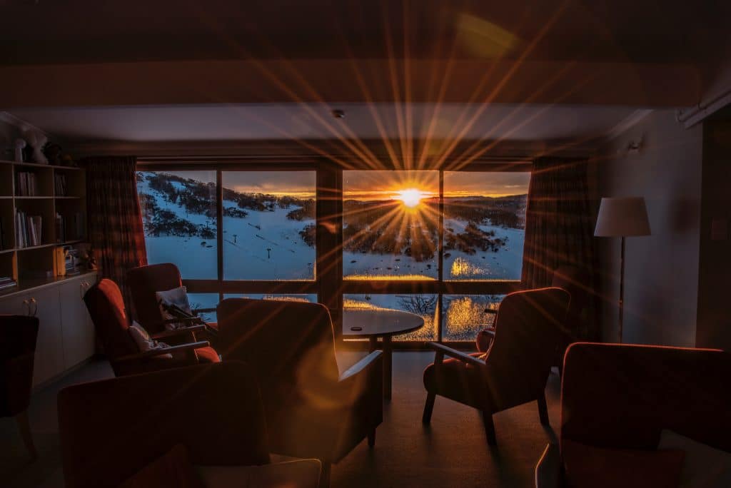 sunset over mountains as seen through a set of large windows in a home's living room