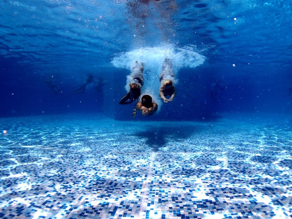 an underwater shot of 3 people diving into a swimming pool