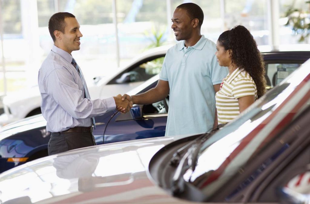 A couple shaking hands as they buy a car at a dealership