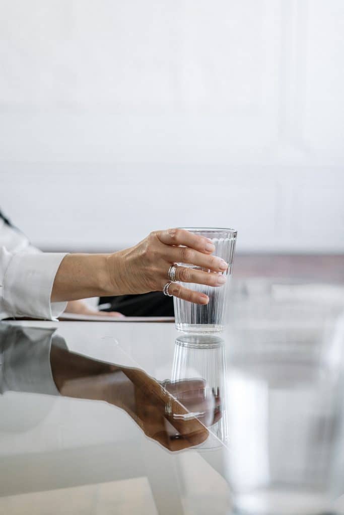 woman's hand holding a glass of water over a glass top table