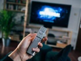 person holding TV remote with a show starting in the background