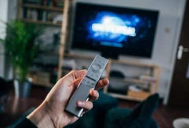 person holding TV remote with a show starting in the background