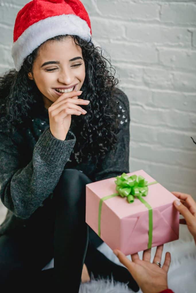 woman wearing a santa claus hat accepting a gift with a smile.