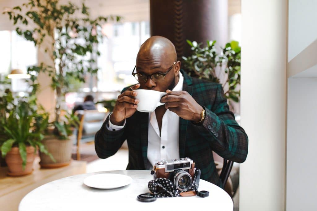 man drinking coffee at a small table with a camera sitting on the table