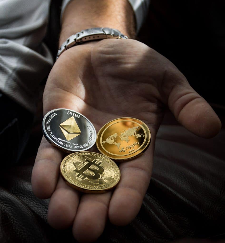 man's hand holding one coin each of ethereum, bitcoin, and ripple