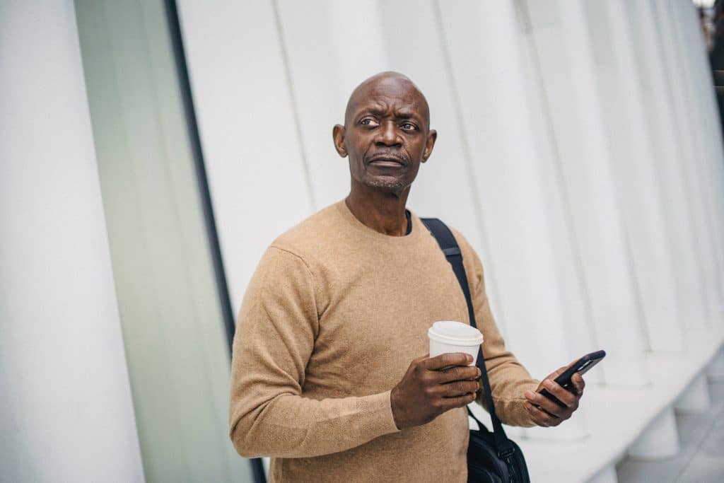 older black man holding a phone and a cup of coffee