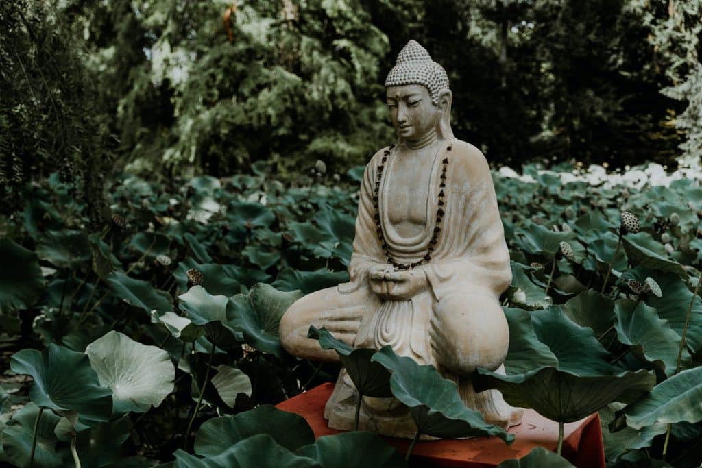 a buddha statue in lotus pose sitting in a garden