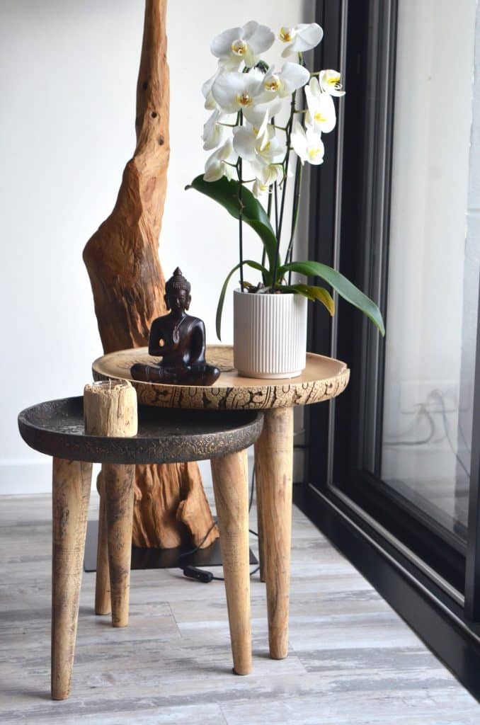 small buddha statue on a decorative wooden table next to orchids