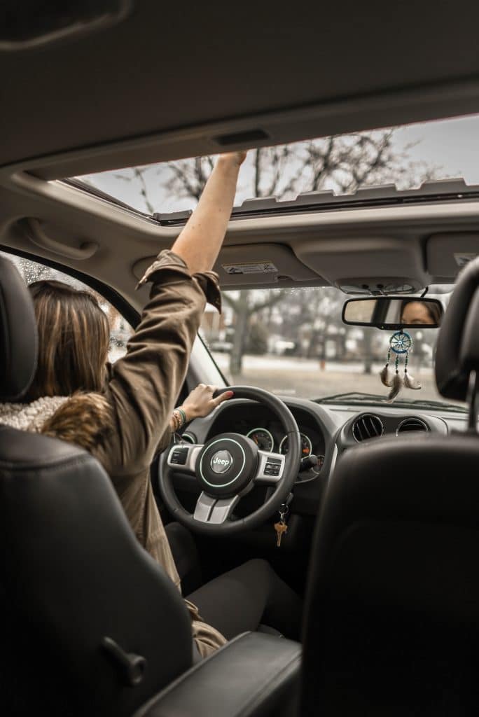 woman putting her hand out of the sunroof while driving