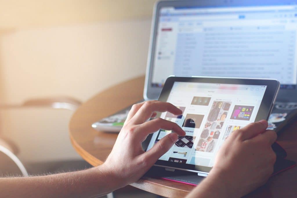 a person's hands working on a tablet, while checking email on a laptop