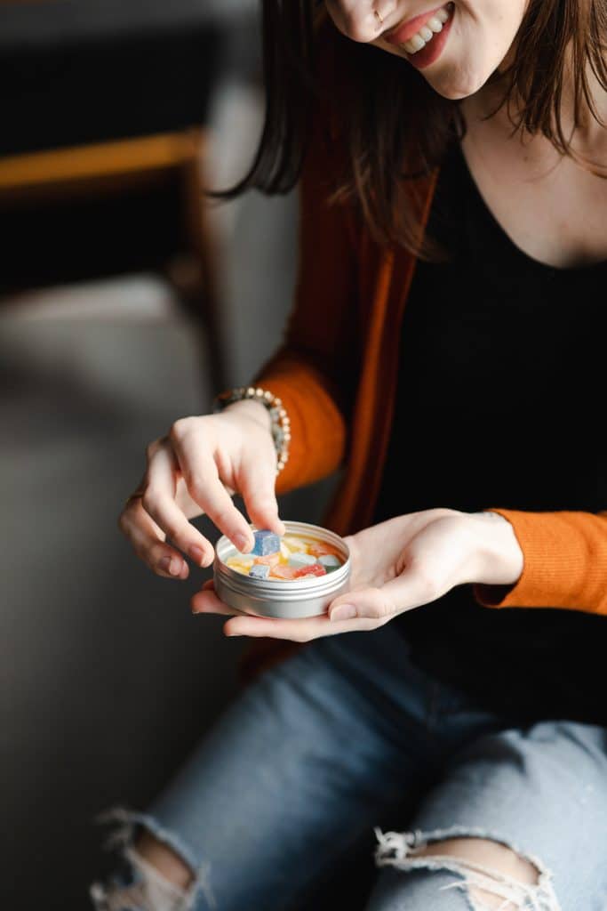 a woman pulling out a cannabis gummy from a tin