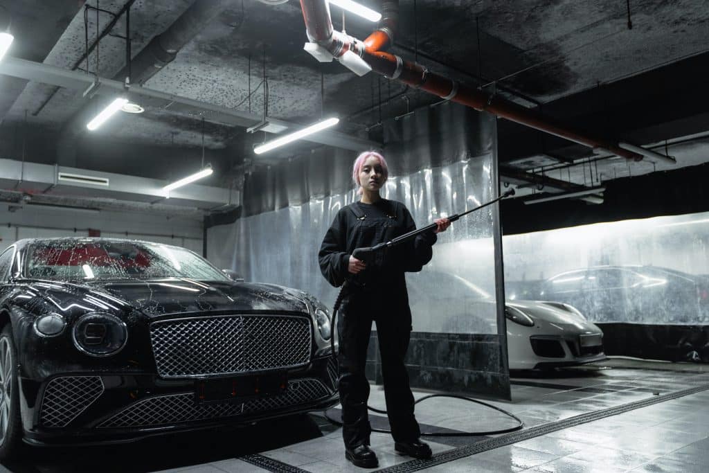 woman holding a cleaning wand while standing in front of a car in a car wash station.