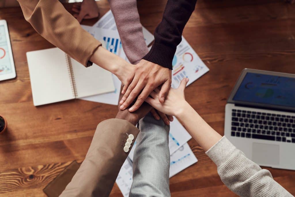 team of people putting their hands in a circle together over a conference room table