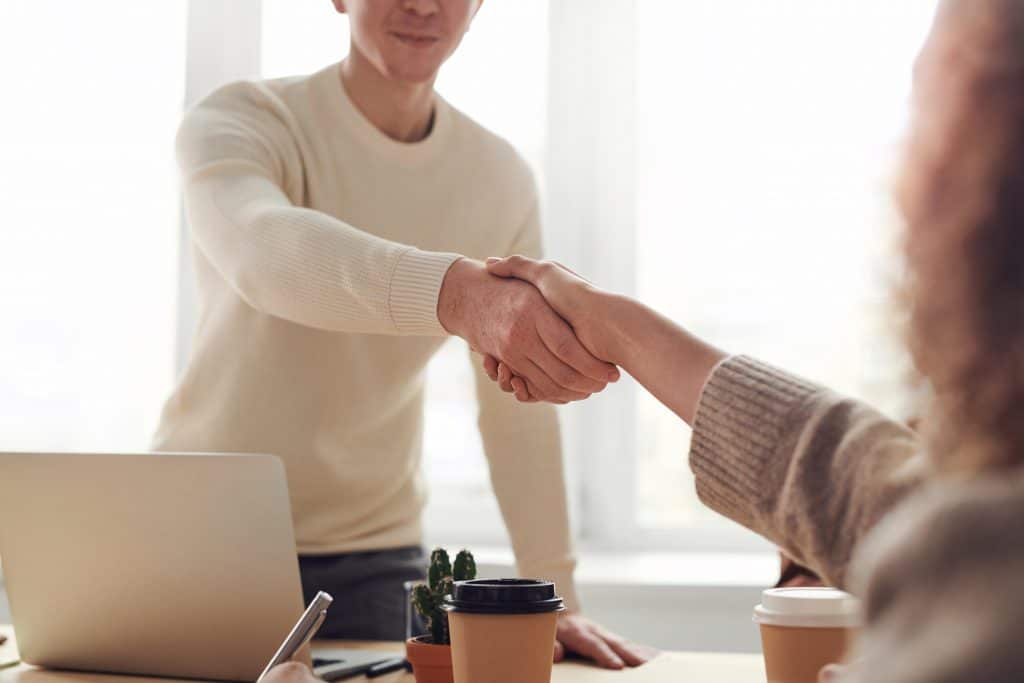 man standing behind a desk, reaching over to shake a woman's hand