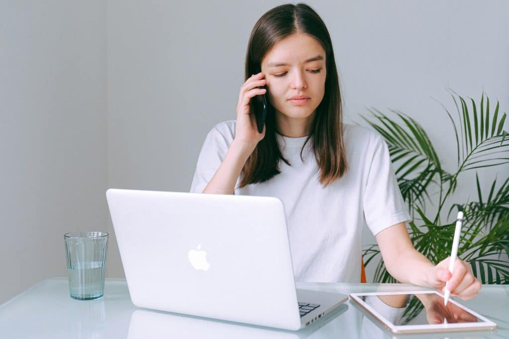 woman taking notes on a tablet while sitting and talking on a phone