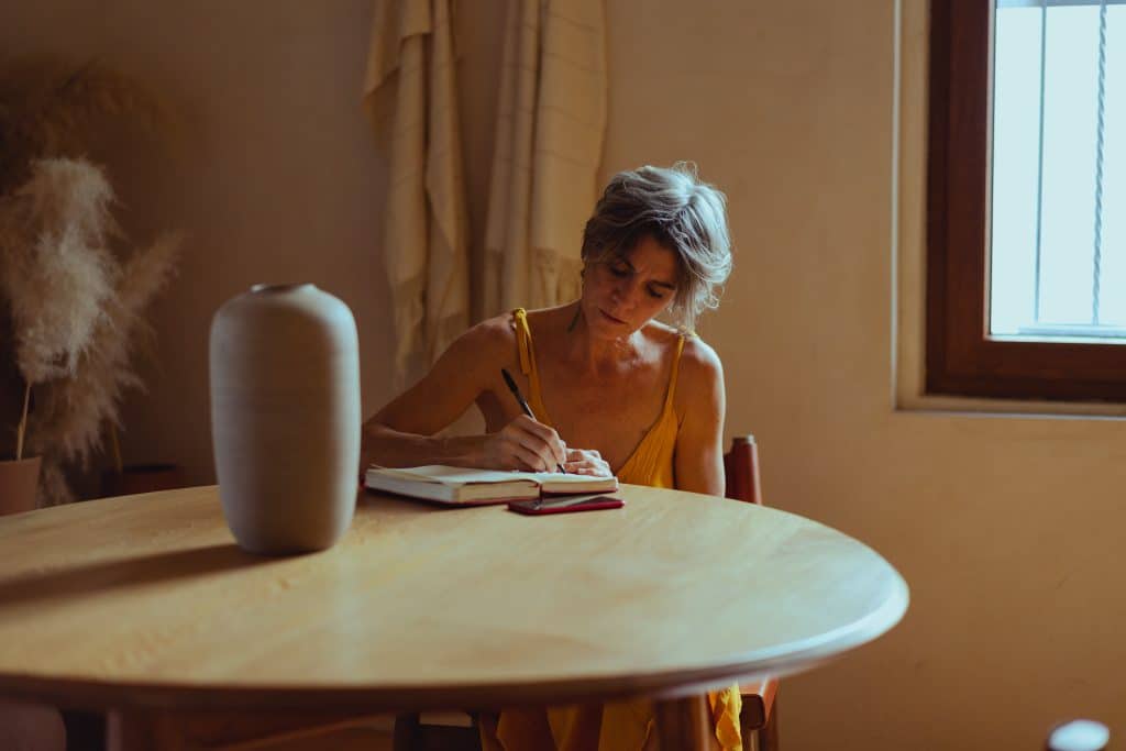 older woman writing in a journal at a wooden table