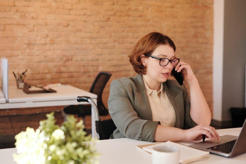 a woman making a phone call while working on her laptop in an office