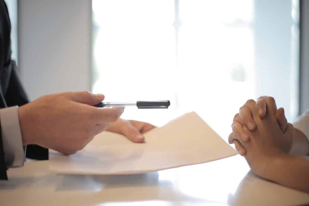 man handing a pen and document to someone to sign.