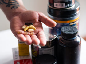 man's hand holding pills with pill bottles in background