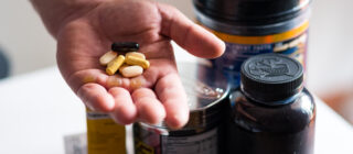 man's hand holding pills with pill bottles in background