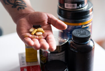 man's hand holding pills with pill bottles in background