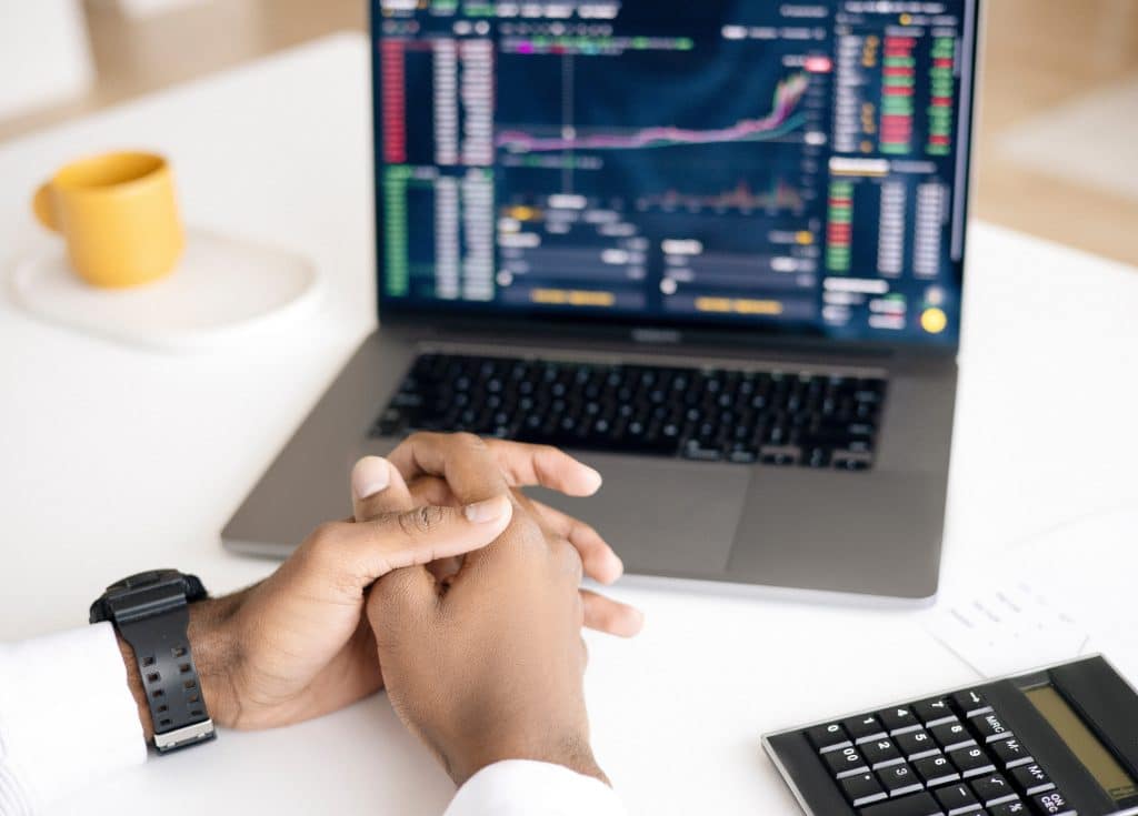 man's hands folded in front of laptop that is displaying an investment trading dashboard