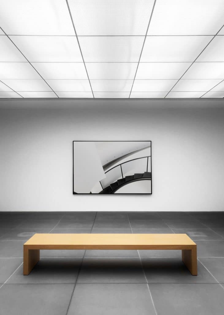 a minimalist wooden bench sitting in front of a black and white art piece.