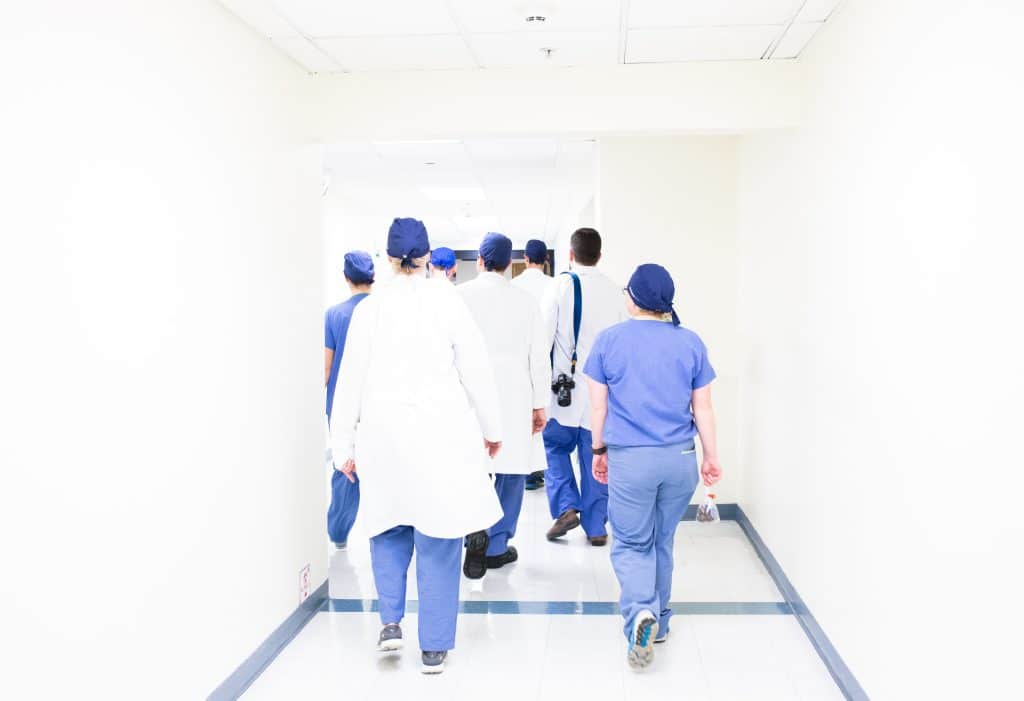 doctors and nurses walking along a white hospital hallway