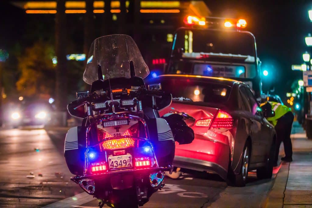 motorcycle cop talking to the driver of a car that is being towed after an accident at night