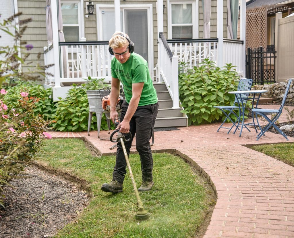man using a weed trimmer around a patio and garden bed area