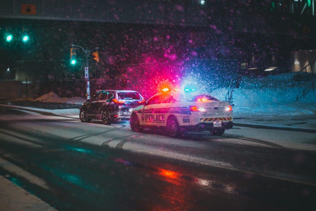 police car pulling another car over during a snow storm