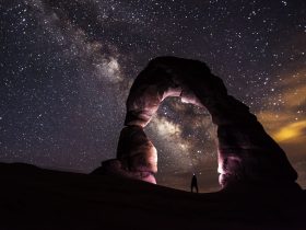 person standing under a rock formation on a starry night
