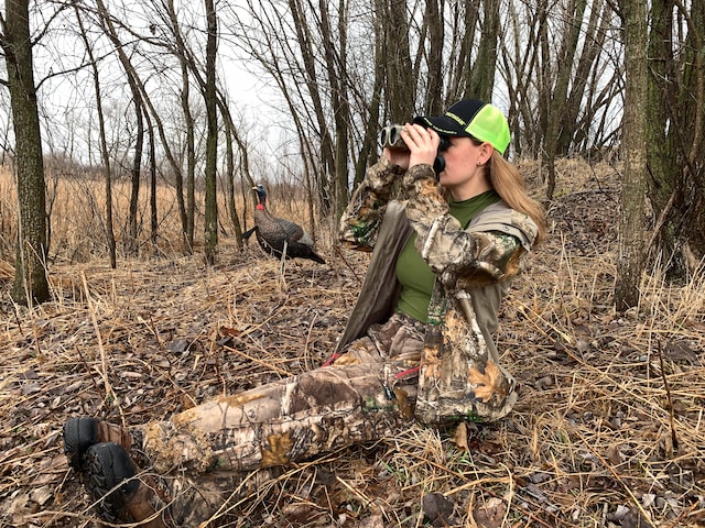 female hunter looking through binoculars with a turkey decoy next to her