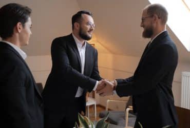 two men shaking hands with a third man watching in the meeting room