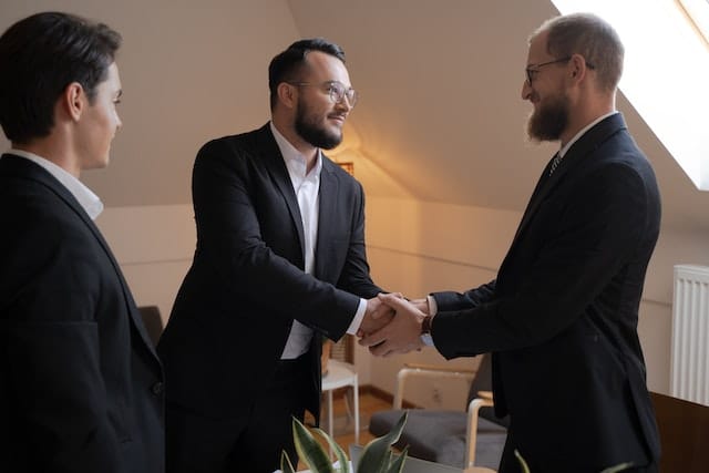 two men shaking hands with a third man watching in the meeting room