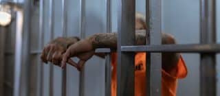 prisoner behind prison bars wearing orange jumpsuit