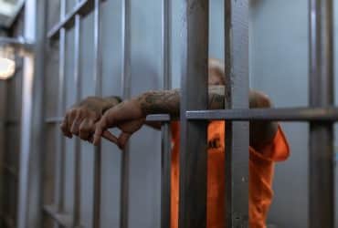 prisoner behind prison bars wearing orange jumpsuit