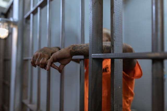 prisoner behind prison bars wearing orange jumpsuit