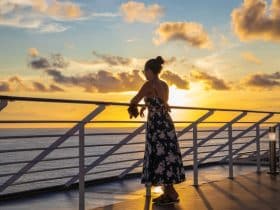 woman looking at sunset while standing on a cruise ship