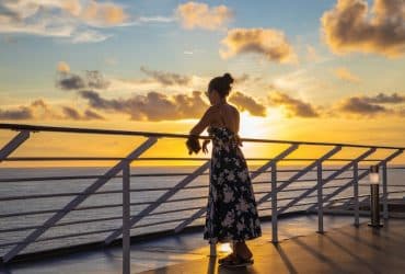 woman looking at sunset while standing on a cruise ship