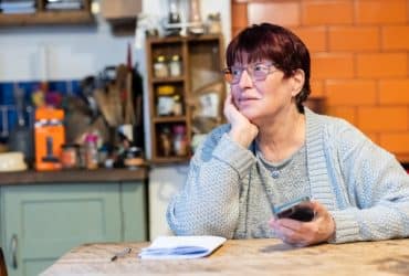 elderly woman at a table with a notebook and smartphone