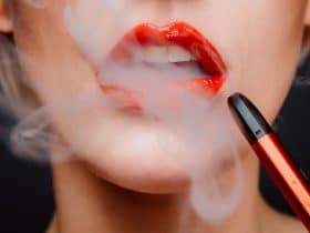 woman's lower face shown exhaling vapor from her mouth while holding a vape pen
