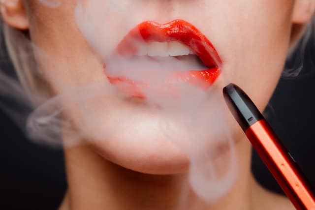 woman's lower face shown exhaling vapor from her mouth while holding a vape pen