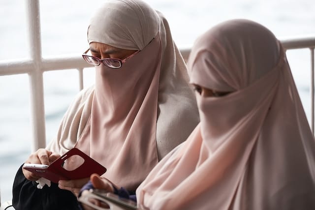 two women in burkas, looking their phones