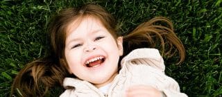 little girl laying in the grass with a big smile