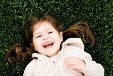 little girl laying in the grass with a big smile