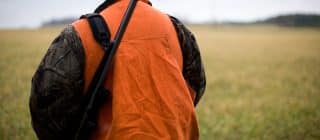 hunter wearing a blaze orange vest and carrying a firearm over his shoulder