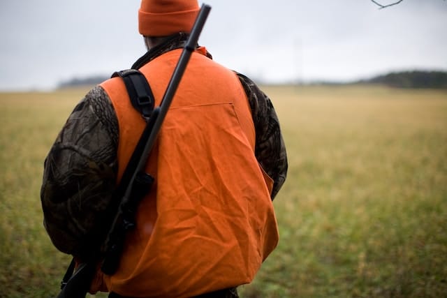 hunter wearing a blaze orange vest and carrying a firearm over his shoulder